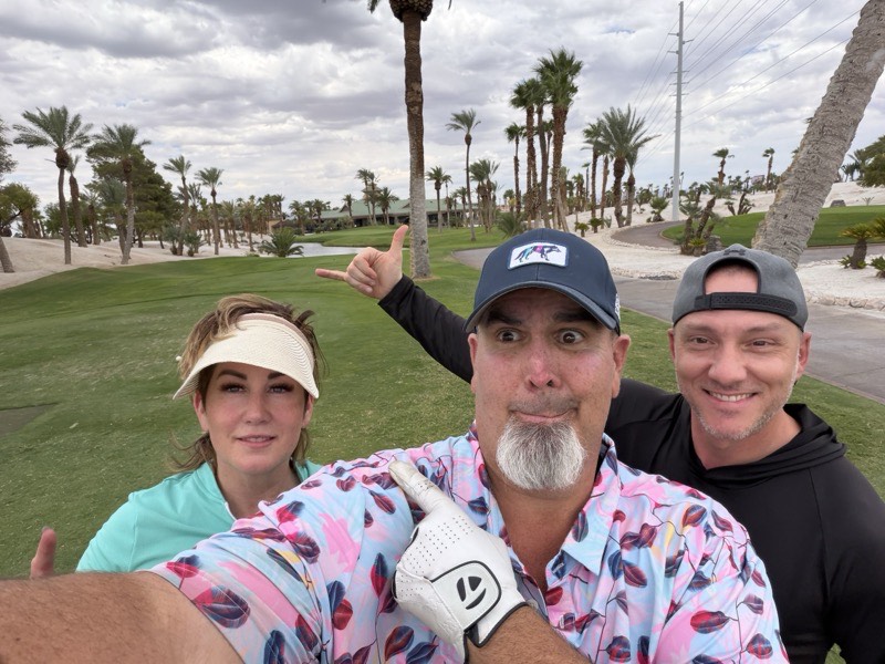 Four people on a golf course under an overcast sky with palm trees.
