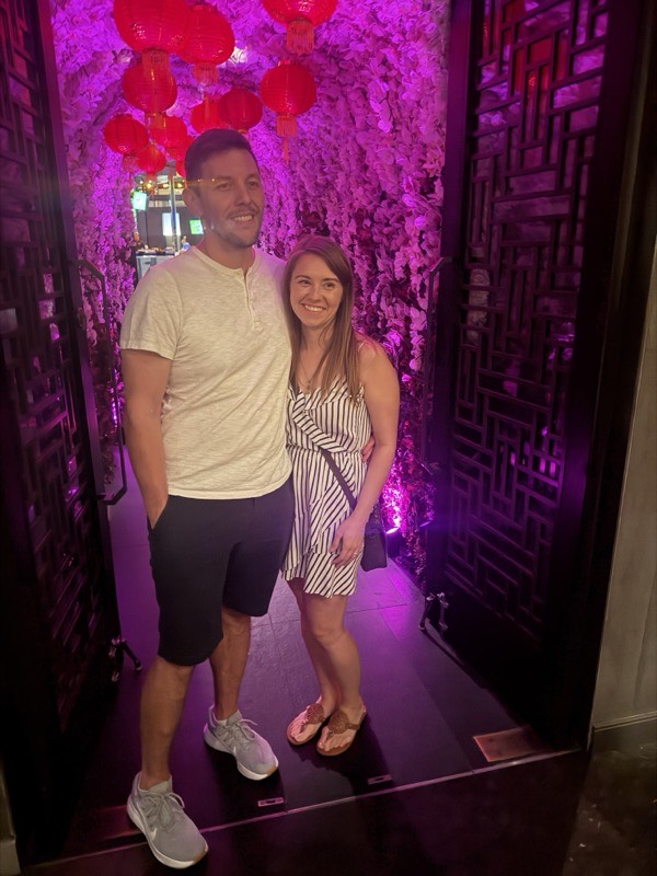 Two people in a corridor lit deep magenta with a red sculptural installation.