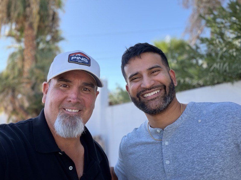Two people outdoors with palm trees behind them.